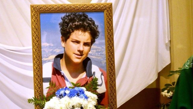 A framed portrait of Carlo Acutis in a church, showing the teenager in a red polo shirt