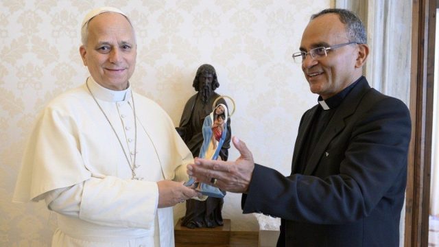 Pope Leo XIV holding a small wooden statue of Our Lady of the Amazon presented to him at the Vatican