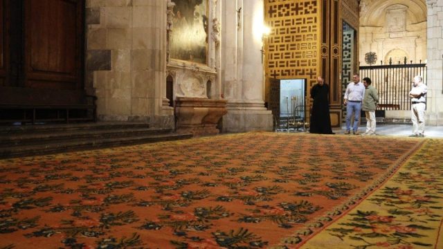 A large 18th-century carpet with floral and fruit patterns on a pink ground, laid out on display inside Murcia Cathedral
