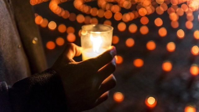 A lit candle beside flowers on a gravestone during All Saints' Day observances