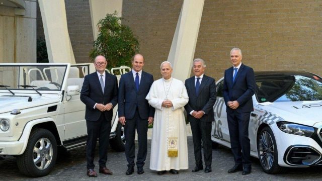 Pope Leo XIV beside a popemobile at the Vatican