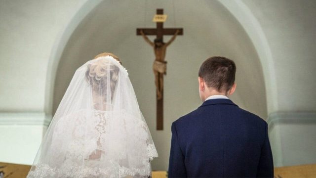 A Catholic couple at their wedding before a priest, with an image of the pope