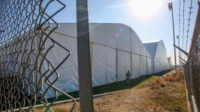 A group of migrants waiting behind a metal fence near the US border